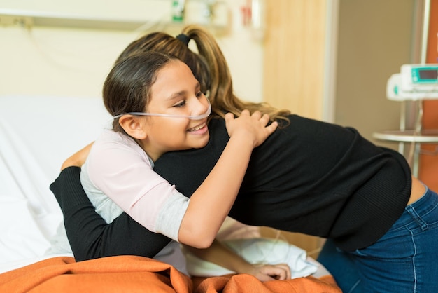Madre abrazando a su hija enferma durante el tratamiento en el hospital y sonriendo