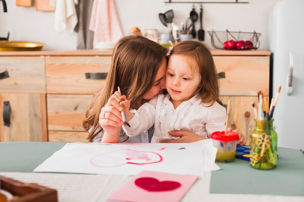 Madre abrazando a su hija mientras ella pinta corazón