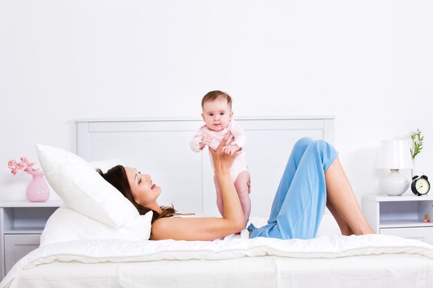 Madre acostada en la cama y jugando con el bebé