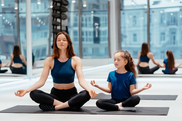 Madre adulta joven y pequeña hija juntas practicando yoga