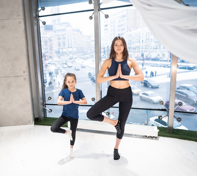 Madre adulta joven y pequeña hija juntas practicando yoga