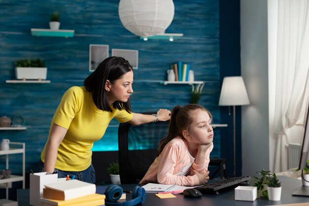 Madre adulta viendo niña haciendo tareas escolares