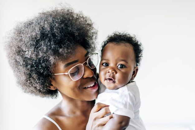 Madre afroamericana cuidando y amando a su bebé contra una superficie blanca