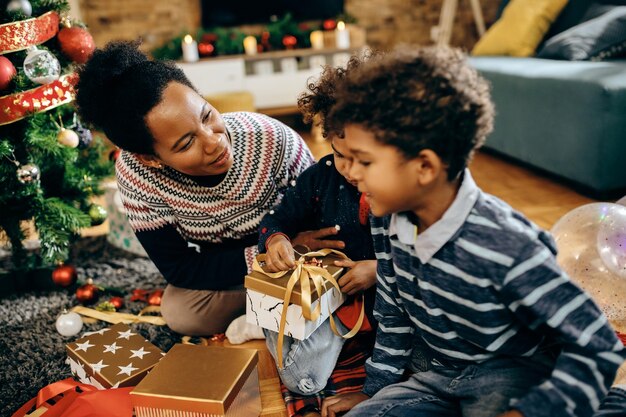 Madre afroamericana hablando con sus hijos mientras abre regalos de Navidad en casa