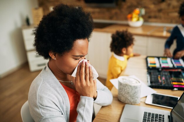 Madre afroamericana sonándose la nariz mientras trabaja en casa