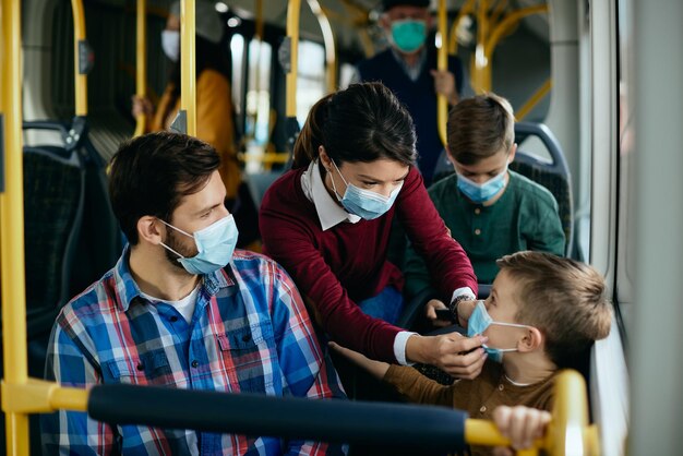 Madre ajustando las máscaras de su hijo mientras viaja en autobús público