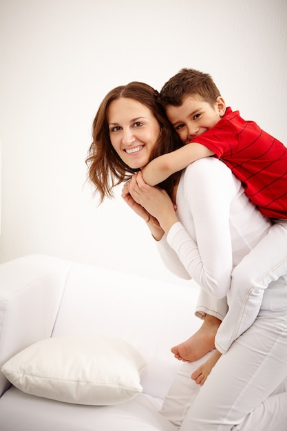 Madre alegre llevando al niño pequeño en la espalda