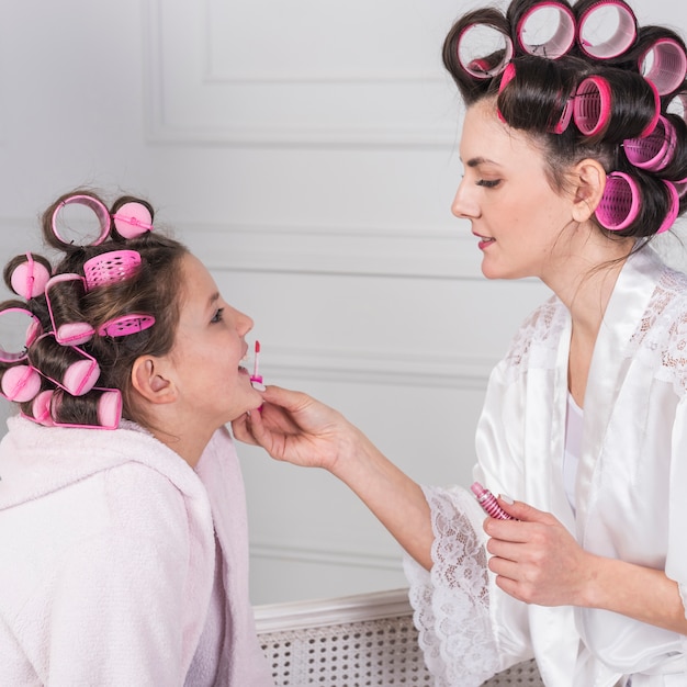 Madre aplicando brillo de labios en labios de hijas.