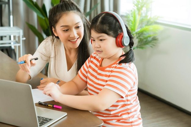 La madre asiática disfruta enseñando y explicando la tarea a su hija para estudiar en línea durante la educación en el hogar en casa en cuarentena en casa aprendiendo en línea un nuevo estilo de vida normal