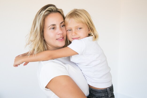 Madre atractiva caucásica sosteniendo hija y mirando a otro lado