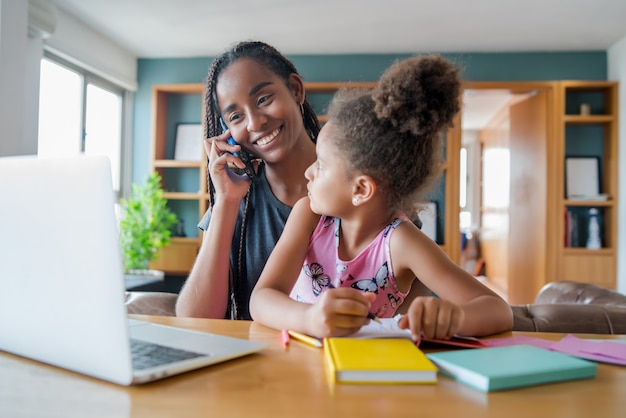 Madre ayudando y apoyando a su hija con la escuela en línea mientras habla por teléfono en casa. Nuevo concepto de estilo de vida normal. Concepto monoparental.