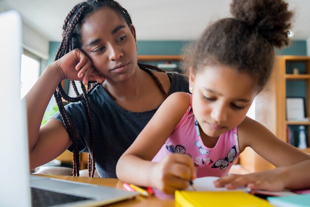 Madre ayudando y apoyando a su hija con la escuela en línea mientras se queda en casa. Nuevo concepto de estilo de vida normal. Concepto monoparental.