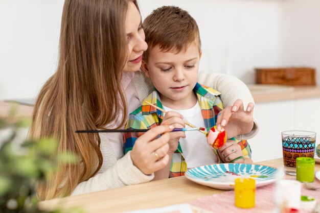 Madre ayudando a hijo a pintar huevos