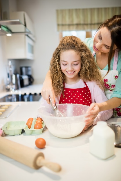 Madre ayudando a su hija en batiendo la harina en la cocina