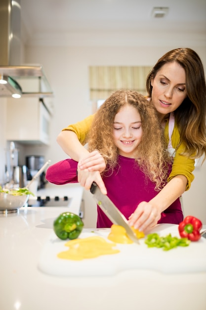 Madre ayudando a su hija en cortar las verduras en la cocina