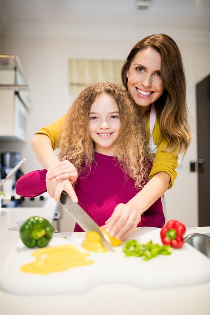 Madre ayudando a su hija en cortar las verduras en la cocina