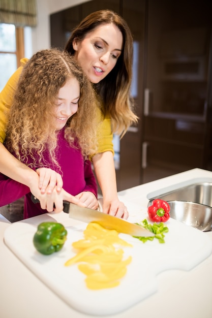 Madre ayudando a su hija en cortar las verduras en la cocina