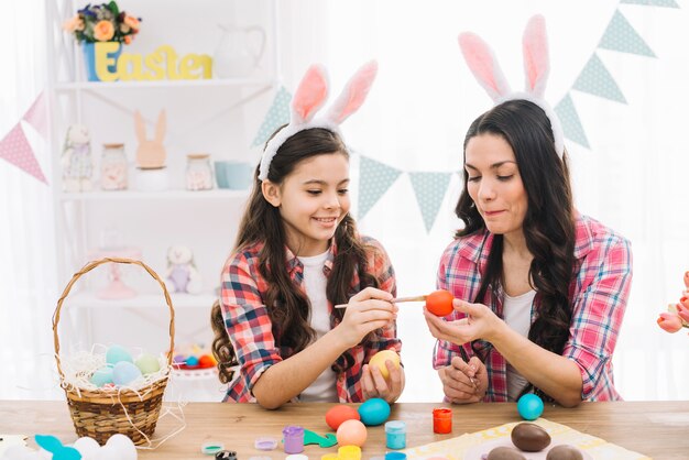 Foto gratuita madre ayudando a su hija a pintar el huevo de pascua en casa