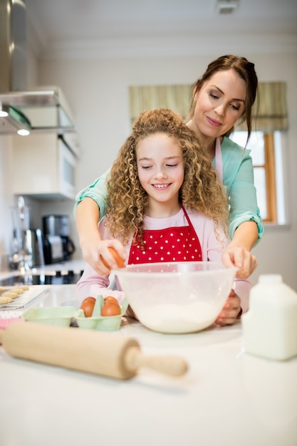 Madre ayudando a su hija en romper los huevos en la cocina