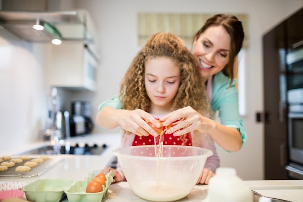 Madre ayudando a su hija en romper los huevos en la cocina