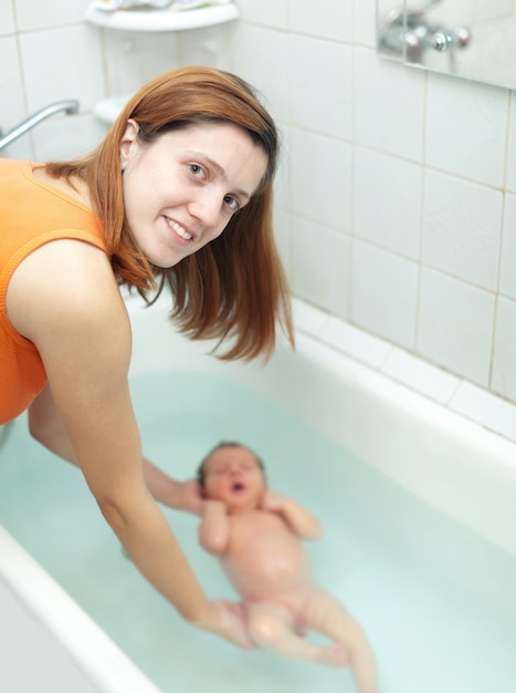 La madre baña al bebé recién nacido en el baño