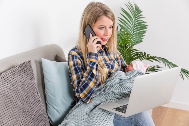 Foto gratuita madre con bebé hablando por teléfono y usando laptop