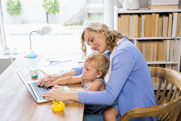 La madre y del bebé que usa la computadora portátil