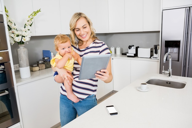 Madre y bebé que usa la tableta digital en la cocina