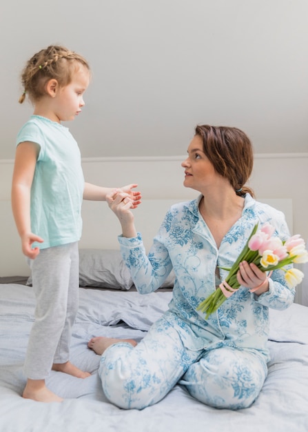 Madre bonita e hija que se miran en la cama que sostiene las flores