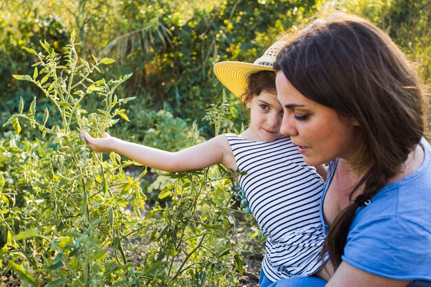 Madre cargando a su hija tocando plantas en el jardín