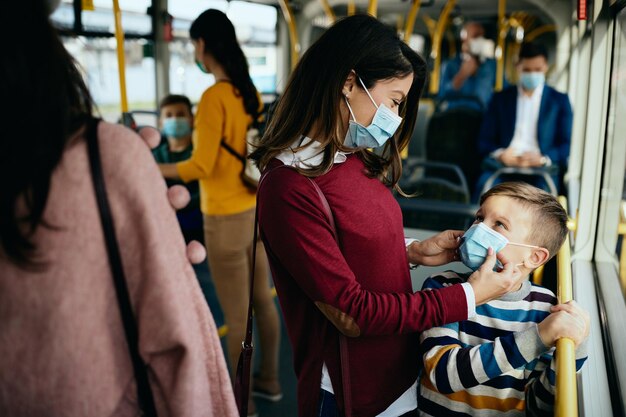 Madre cariñosa ajustando la mascarilla de su hijo mientras viaja en autobús