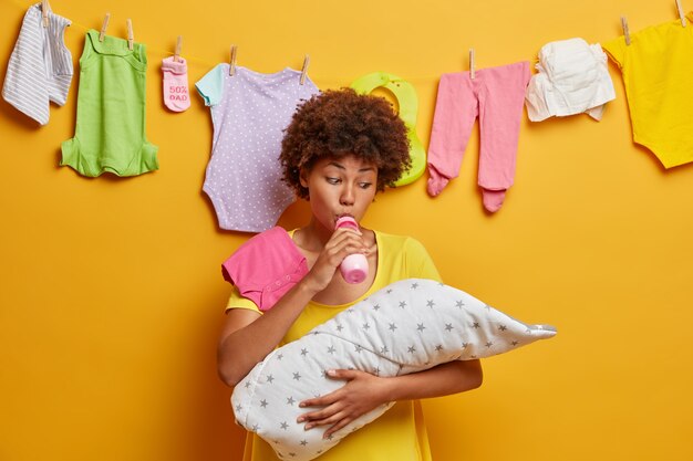 Una madre cariñosa alimenta al bebé con un biberón de leche, chupa el pezón, sostiene en las manos al bebé envuelto en una manta y se ocupa de la nutrición del niño. Recién nacido siendo alimentado por mamá. Niñera ocupada posa con hijo pequeño