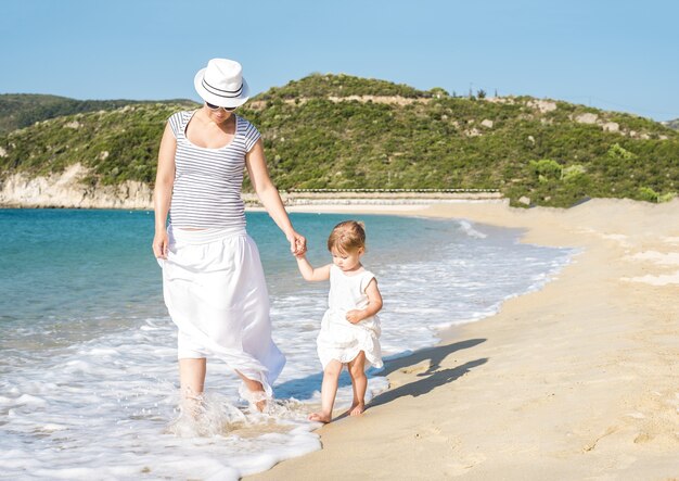 Madre caucásica caminando por la playa con su hija durante el día