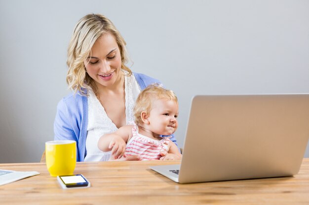 Madre celebración niña mientras que usando la computadora portátil