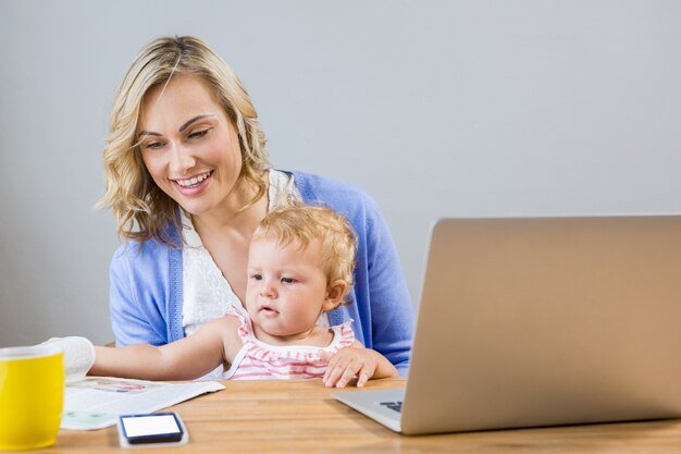 Madre celebración niña mientras que usando la computadora portátil