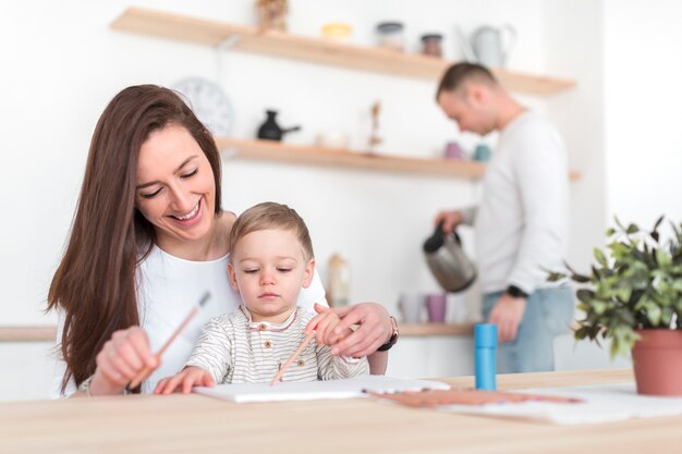 Madre en la cocina con niño y padre desenfocado