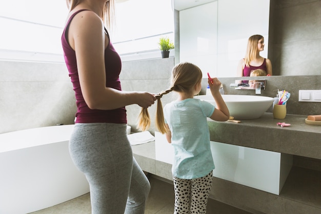 Madre de la cosecha hija de trenzado en el baño