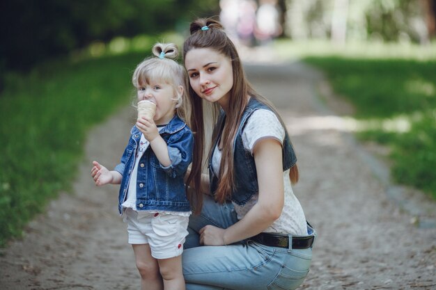 Madre en cuclillas con su hija mientras esta se come un helado con el fondo desenfocado