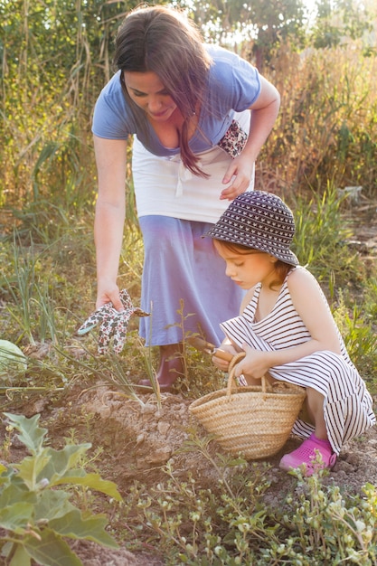 Madre dando guantes a su hija sosteniendo una paleta sentada en el campo