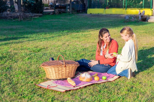 Madre dando una manzana a su hija en el parque