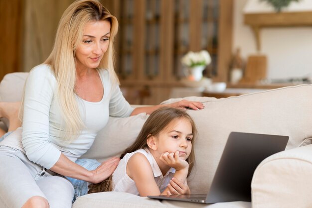 Madre dejando que su hija mire su computadora portátil mientras trabaja desde casa