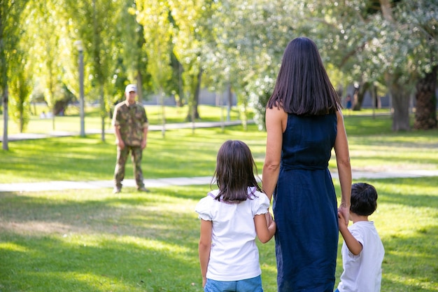 Madre con dos hijos que conocen al padre militar al aire libre. Vista trasera. Concepto de reunión familiar