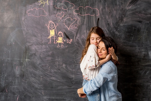 Madre e hija abrazando cerca de pizarra con dibujo
