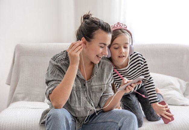 Madre e hija alegres descansan en casa, escuchando música en auriculares