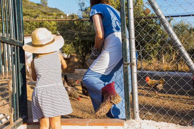 Madre e hija alimentando pollos en la granja