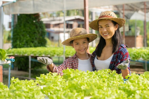 Madre e hija asiáticas están ayudando juntas a recolectar la verdura hidropónica fresca en la granja, el concepto de jardinería y la educación infantil de la agricultura doméstica en el estilo de vida familiar.