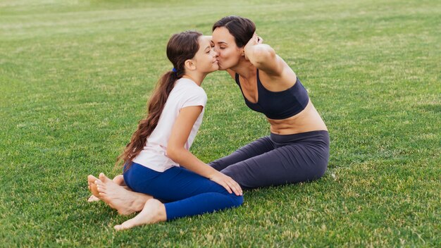 Madre e hija besándose y haciendo ejercicio en la naturaleza.