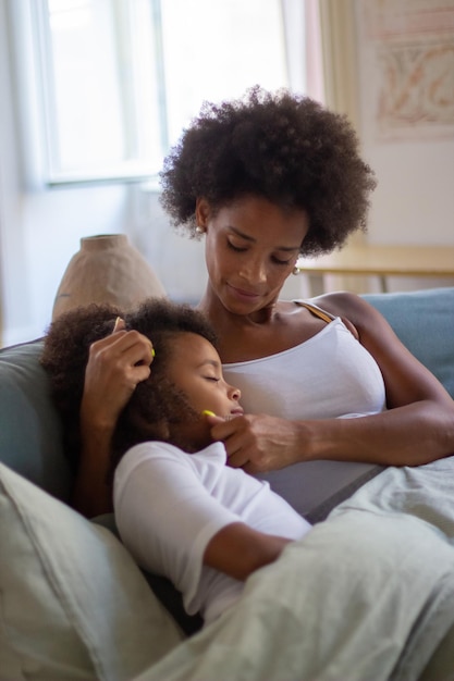 Madre e hija con cabello rizado en la cama. Mujer afroamericana y niña somnolienta sentada, apoyada en el hombro, con los ojos cerrados. Familia, paternidad, concepto de hogar.