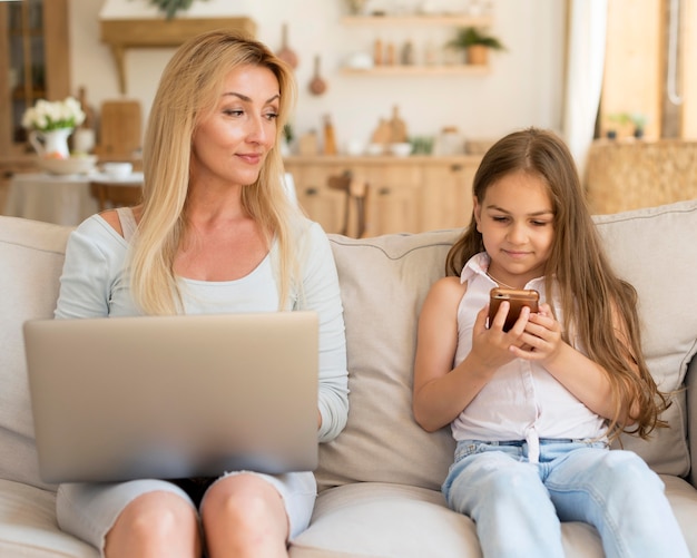 Madre e hija en casa con laptop y smartphone