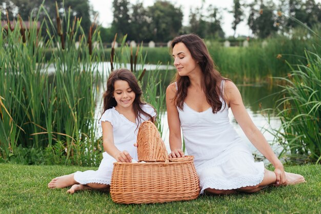 Madre e hija con cesta de picnic junto al lago.